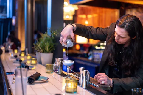 A bartender pouring a cocktail into a coupe glass